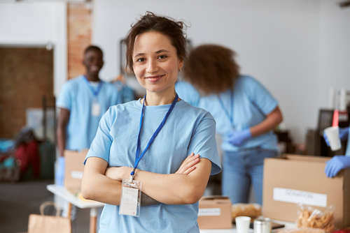 A Connecticut Blood Center volunteer standing in a blue shirt with her arms crossed smiling at a blood drive.